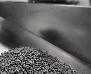 Metal injection molding (MIM) feedstock pellets on stainless steel surface, used in precision manufacturing of complex metal components
